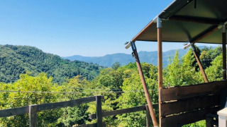 Vista dalla terrazza di una tenda safari sulle colline verdi con cielo azzurro, atmosfera rilassante.