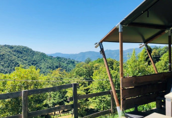 Vista dalla terrazza di una tenda safari sulle colline verdi con cielo azzurro, atmosfera rilassante.