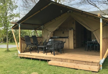 Foto esterna di una tenda safari con veranda in legno, area relax e cucina con servizi igienici.