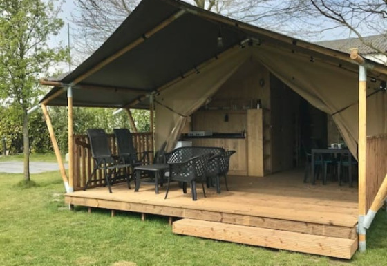 Buitenzicht van een safaritent met houten terras, zithoek en binnenkeuken met sanitaire voorzieningen.