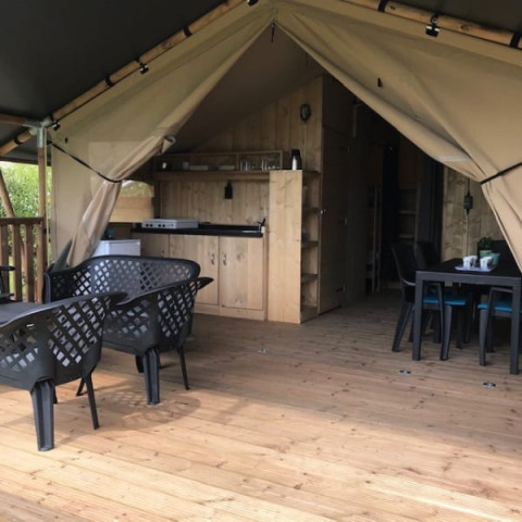 Vista interior de una tienda safari con terraza de madera, comedor, sillas y cocina en Camping de Zwammenberg.