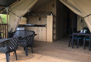 Vista interna di una tenda safari con pavimento in legno, tavolo da pranzo, sedie e cucina a Camping de Zwammenberg.