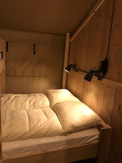 Vista interior de una tienda Safari con cama cómoda y lámpara en Camping de Zwammenberg, Países Bajos.