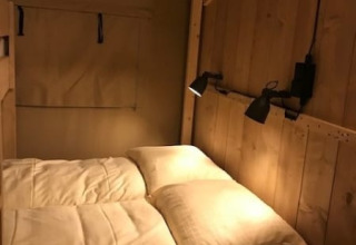 Interior view of a Safari tent with a cozy bed and wall lamp at Camping de Zwammenberg, Netherlands.