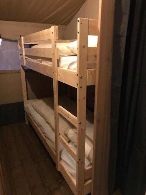 Ein hölzernes Etagenbett im Inneren eines Safarizelts mit schwacher Beleuchtung bei Camping de Zwammenberg.