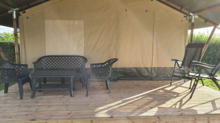 Terraza de tienda safari con muebles de jardín de plástico negro sobre plataforma de madera en entorno natural.