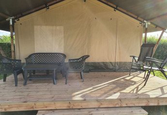 Veranda di tenda safari con mobili da giardino in plastica nera su piattaforma di legno, immersa nel verde.