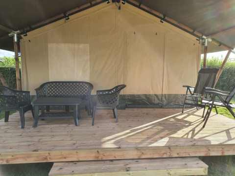 Veranda di tenda safari con mobili da giardino in plastica nera su piattaforma di legno, immersa nel verde.