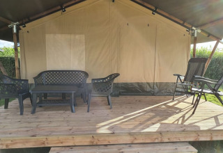 Veranda di tenda safari con mobili da giardino in plastica nera su piattaforma di legno, immersa nel verde.