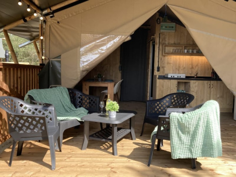 Tenda safari con area salotto e tavolo su terrazza in legno al Parco Ricreativo Keiheuvel, Belgio.