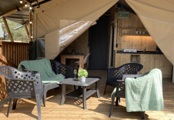 Tenda safari con area salotto e tavolo su terrazza in legno al Parco Ricreativo Keiheuvel, Belgio.
