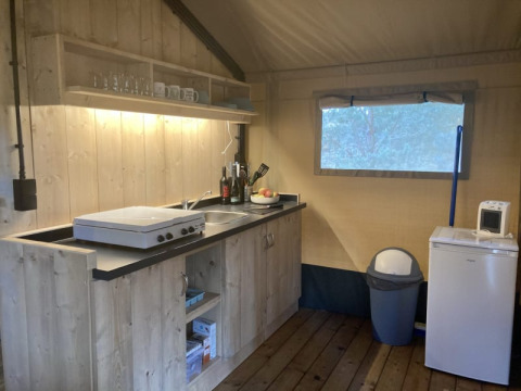 Zona de cocina en tienda safari con armarios de madera, placa de cocción, nevera y microondas en Keiheuvel.