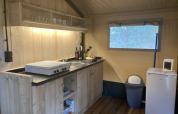 Kitchen area inside a safari tent featuring wood cabinets, cooktop, fridge, and microwave at Keiheuvel Park.