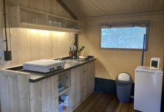 Angolo cucina in tenda safari con mobili in legno, fornello, frigorifero e microonde al Keiheuvel Park.