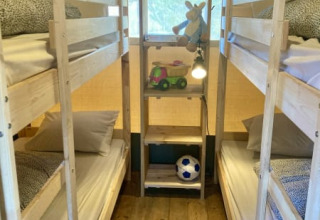 Binnenin een safaritent bij Recreatiepark Keiheuvel, België, met stapelbedden en kinderspeelgoed op rekken.