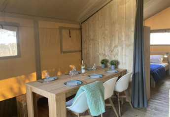 Interior of a safari tent with dining area, chairs, wooden walls, and a bedroom at Recreation Park Keiheuvel.