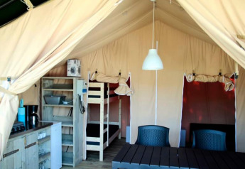 Binnenkant van een safaritent met keukentje, stapelbed, eettafel en stoelen, ideaal voor glamping.