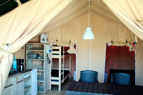 Inde i et safaritelt med køkkenhjørne, køjeseng, bord og stole, ideelt til komfortabel camping.