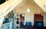 Inde i et safaritelt med køkkenhjørne, køjeseng, bord og stole, ideelt til komfortabel camping.