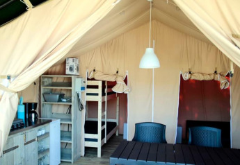 Inde i et safaritelt med køkkenhjørne, køjeseng, bord og stole, ideelt til komfortabel camping.
