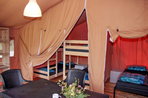 Interior de tienda safari con literas, camas individuales, mesa, sillas y flores decorativas sobre la mesa.