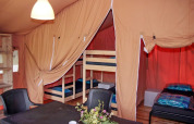 Interieur van een safaritent met stapelbedden, eenpersoonsbedden, tafel, stoelen en bloemen op tafel.