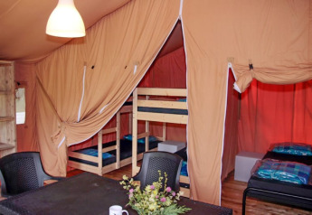 Interior de tienda safari con literas, camas individuales, mesa, sillas y flores decorativas sobre la mesa.