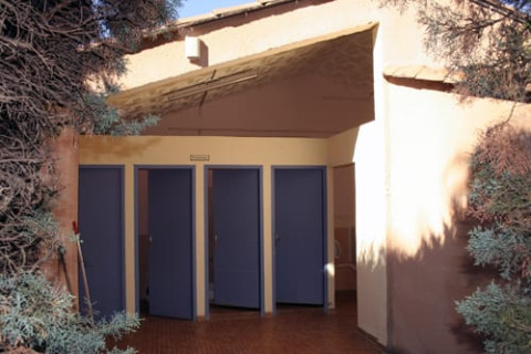 Sanitaires extérieurs près de la tente Safari tent, entourés d’arbustes et d’arbres ensoleillés.