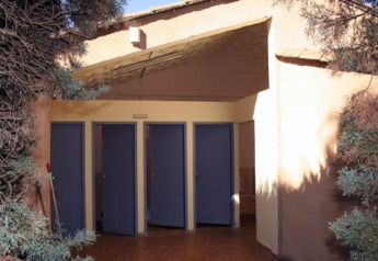 Outdoor restroom near Safari tent called Safari tent, surrounded by bushes and trees in sunlight.