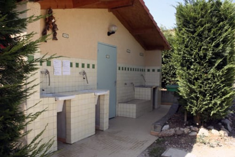 Outdoor washing station at safari tent with tiled sinks, a wooden roof, and greenery on both sides.