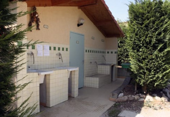 Área de lavado exterior junto a una tienda safari, con fregaderos alicatados y vegetación a los lados.