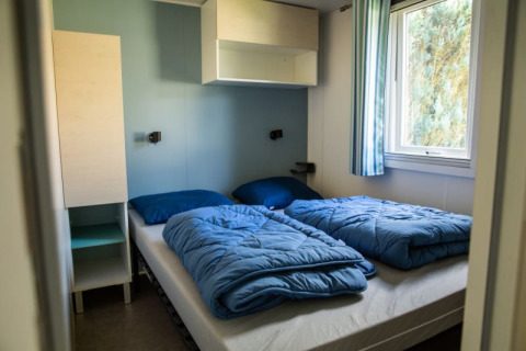 Habitación con dos camas y ropa de cama azul en Sun Lodge, Camping Les Bouleaux, Francia. Decoración simple.