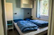 Habitación con dos camas y ropa de cama azul en Sun Lodge, Camping Les Bouleaux, Francia. Decoración simple.