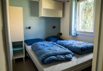 Camera con due letti e biancheria blu al Sun Lodge, Camping Les Bouleaux, Francia. Arredamento semplice.