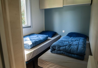 Two single beds with blue comforters in a Sun Lodge room at Camping Les Bouleaux in France.