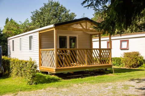 Sun Lodge, una casa móvil moderna con porche de madera, rodeada de un entorno natural y verde.
