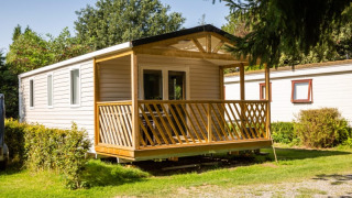 Sun Lodge, a modern mobile home with a wooden porch, nestled in a peaceful, green natural setting.