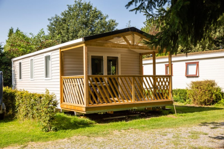 Sun Lodge, a modern mobile home with a wooden porch, nestled in a peaceful, green natural setting.
