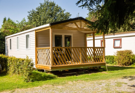 Sun Lodge, a modern mobile home with a wooden porch, nestled in a peaceful, green natural setting.
