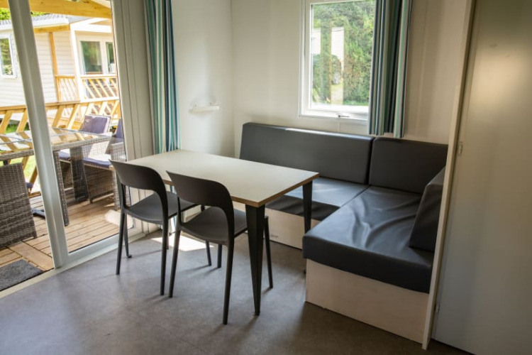 Dining area with table, chairs, and corner sofa inside Sun Lodge at Camping Les Bouleaux, France.