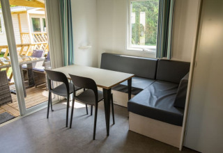 Dining area with table, chairs, and corner sofa inside Sun Lodge at Camping Les Bouleaux, France.