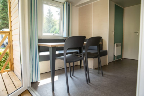Sol lodge interiør med spisebord og stole, vindue med gardiner, og udgang til terrasse i Camping Les Bouleaux.
