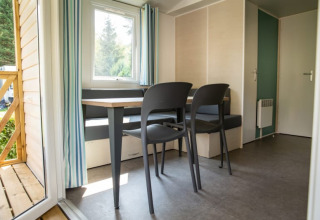 Binnenkant van Sun Lodge op Camping Les Bouleaux in Frankrijk, met zitbank, tafel, stoelen en buitenzicht.