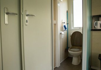 Baño pequeño con inodoro, papel higiénico, escobilla y ventana en Sun Lodge, Camping Les Bouleaux, Francia.