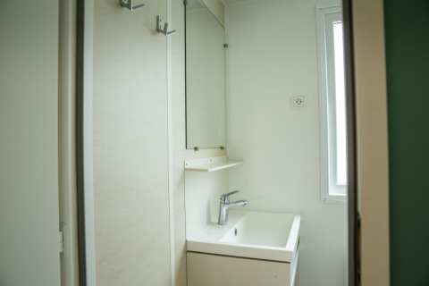 Small, bright bathroom with square sink, mirror, and window inside the Sun Lodge at Camping Les Bouleaux, France.