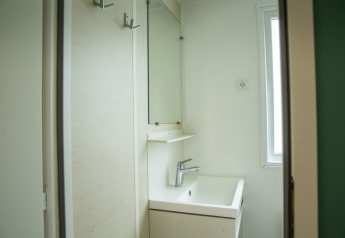 Small, bright bathroom with square sink, mirror, and window inside the Sun Lodge at Camping Les Bouleaux, France.