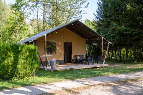 Tienda safari en Camping Les Bouleaux en Francia, con terraza y sillas, rodeada de naturaleza verde.