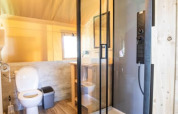 Baño moderno con ducha de vidrio y inodoro en una tienda safari en Camping Les Bouleaux, Francia.