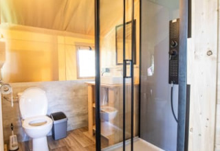 Baño moderno con ducha de vidrio y inodoro en una tienda safari en Camping Les Bouleaux, Francia.