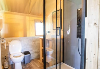 Modern bathroom with glass shower and toilet inside a safari tent at Camping Les Bouleaux, France.